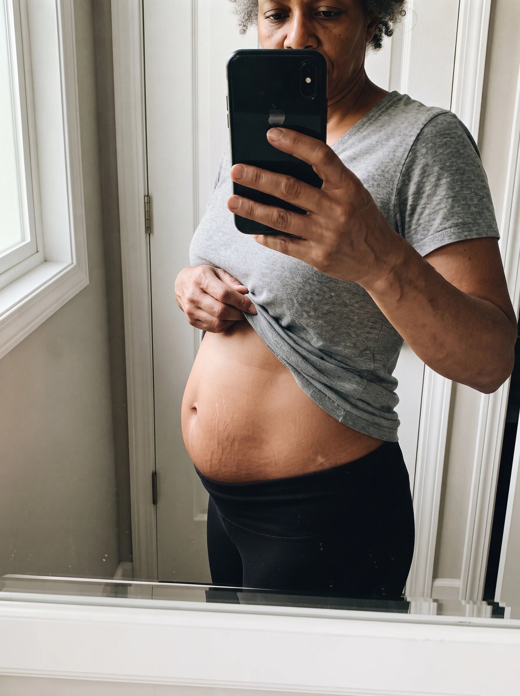 Woman in front of the mirror lifting her shirt and looking at her belly after her pregnancies