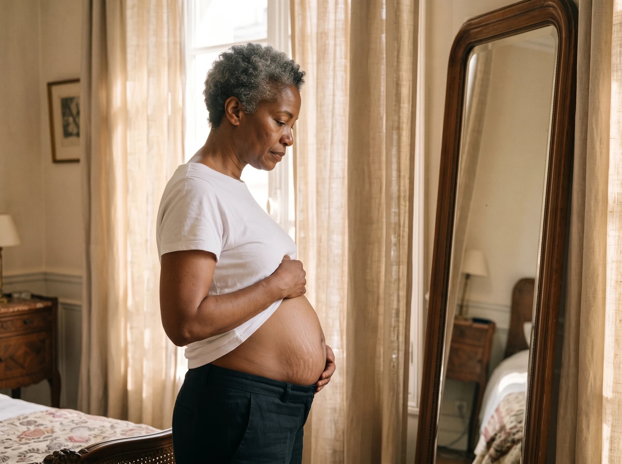 Woman in profile in front of a mirror, hand on her belly